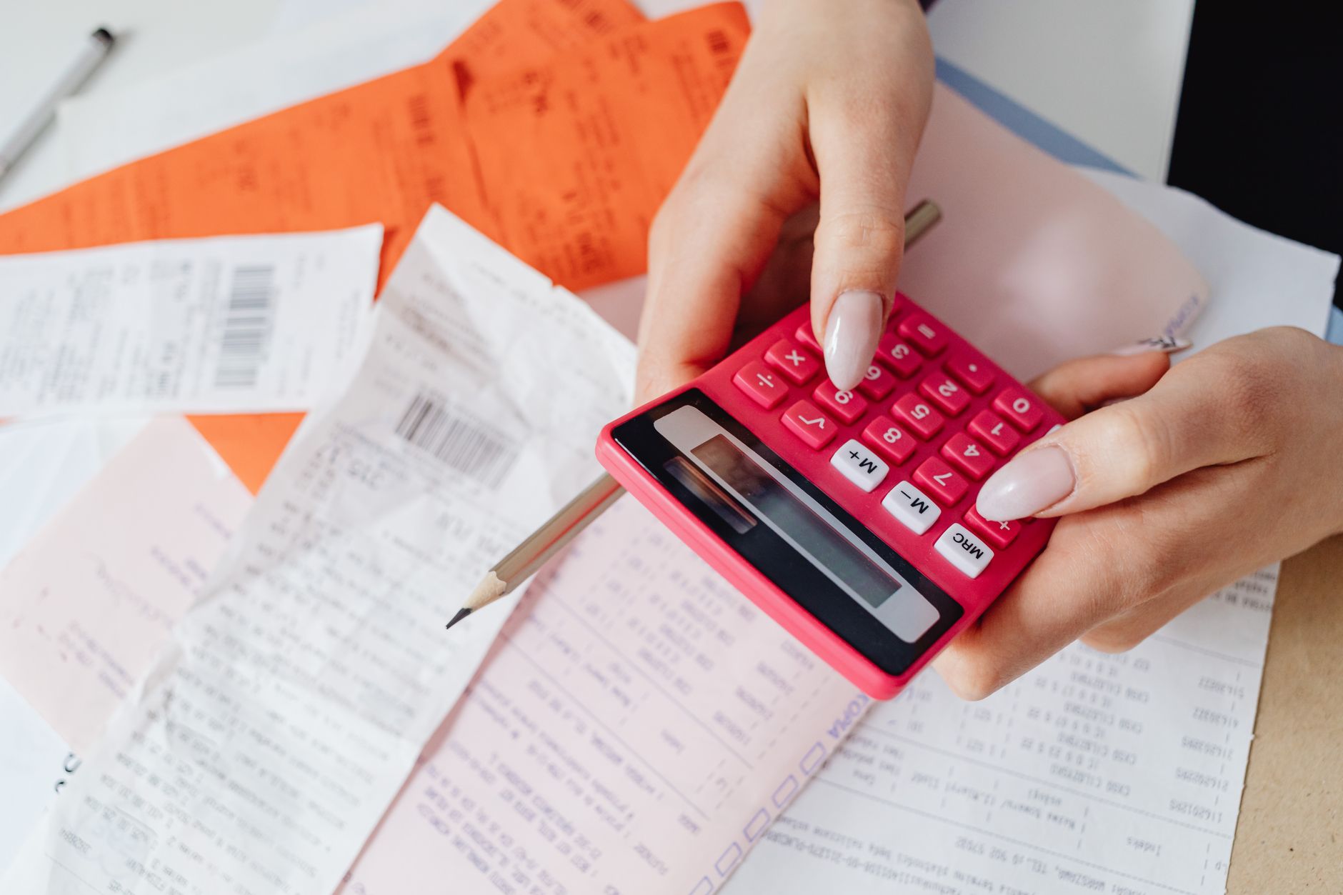 Pesquisa mostra quem mais está deixando de pagar as contas no Brasil e revela a relação entre renda familiar, dificuldade financeira e aumento da inadimplência 1 Mãos usando uma calculadora rosa para gerenciar despesas entre vários recibos e documentos.