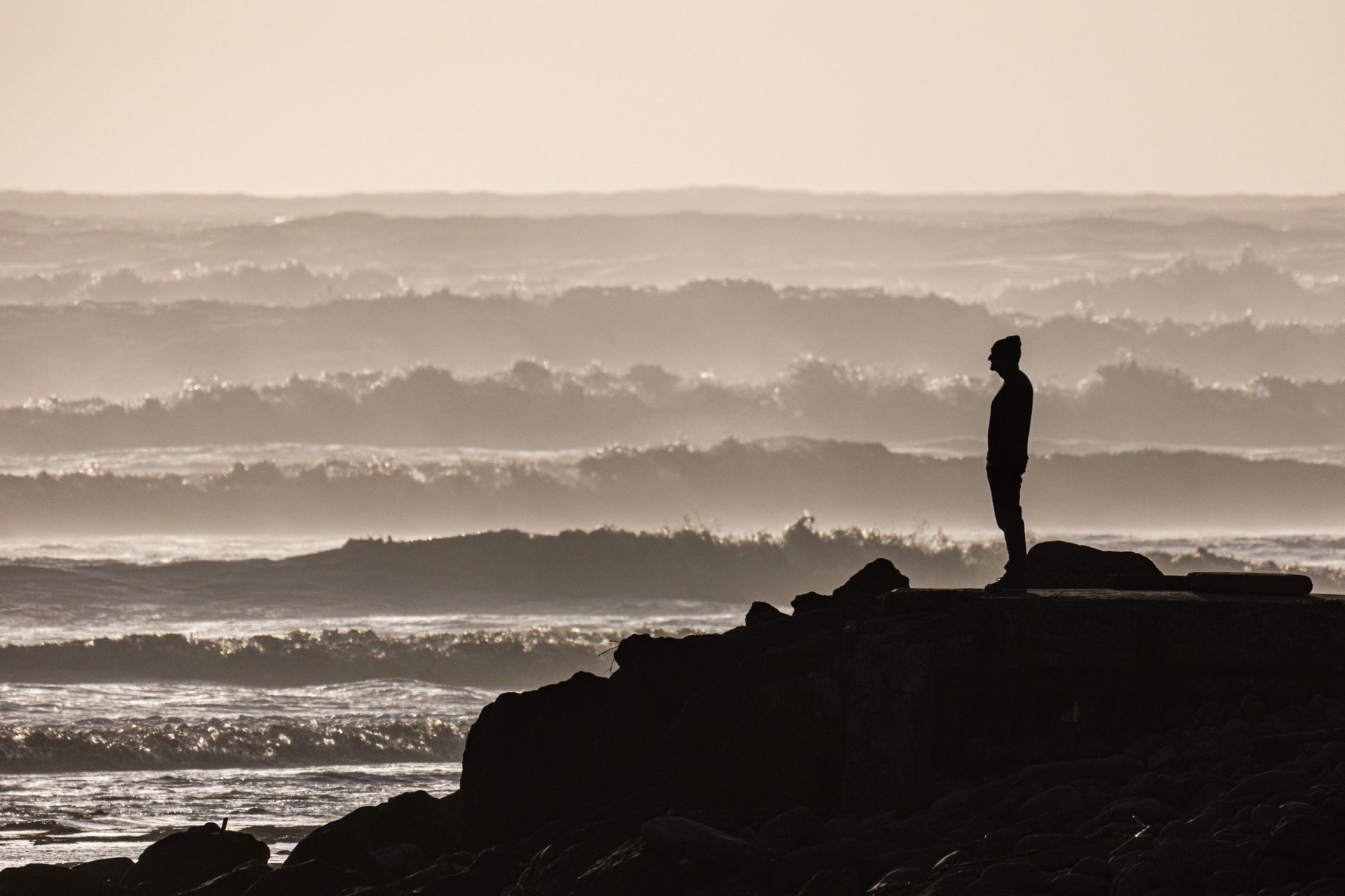 Uma silhueta solitária está ao lado do oceano, observando as ondas ao pôr do sol.