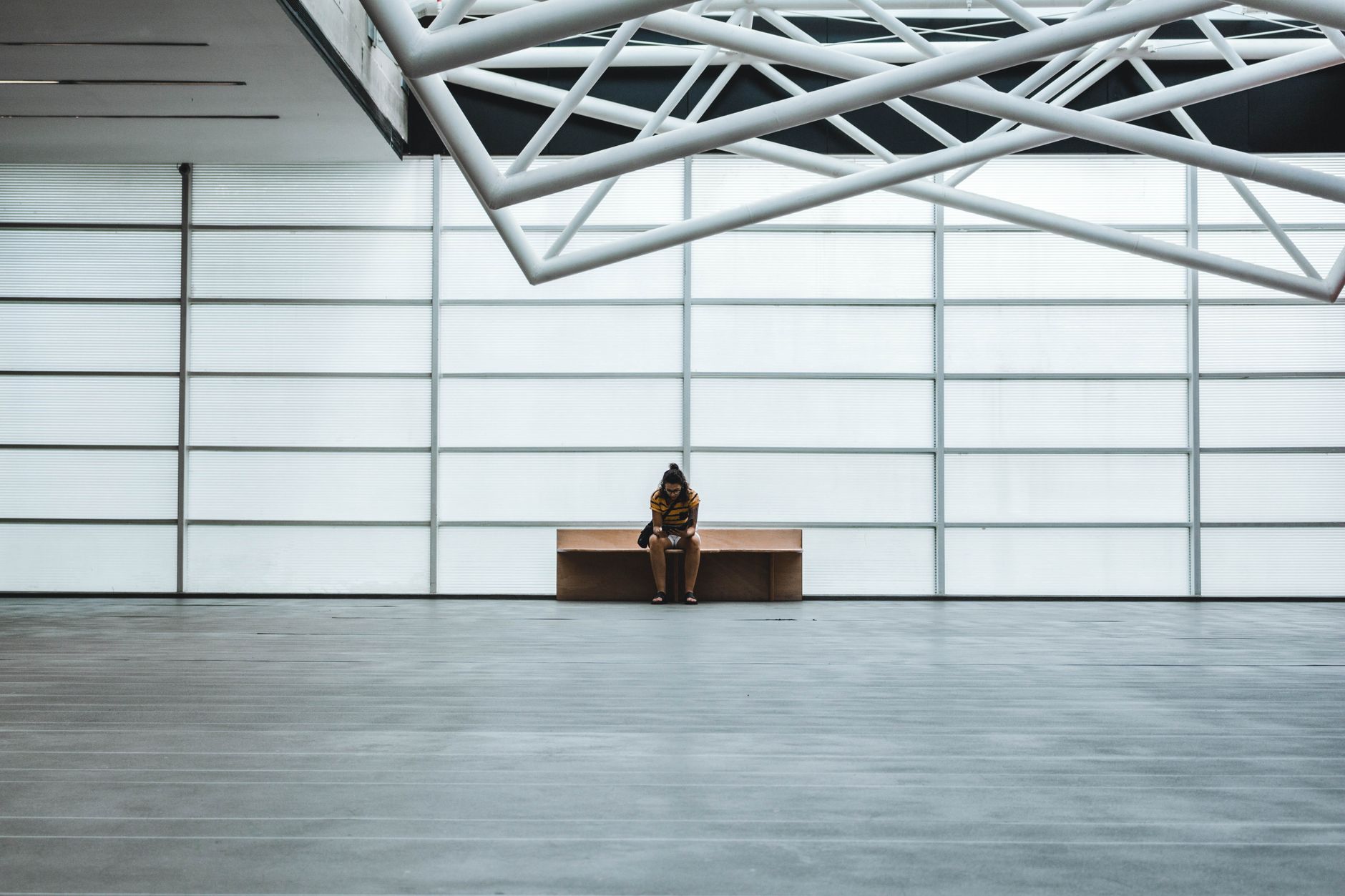 Uma pessoa solitária senta-se em um banco em um interior moderno e espaçoso com design de teto geométrico.