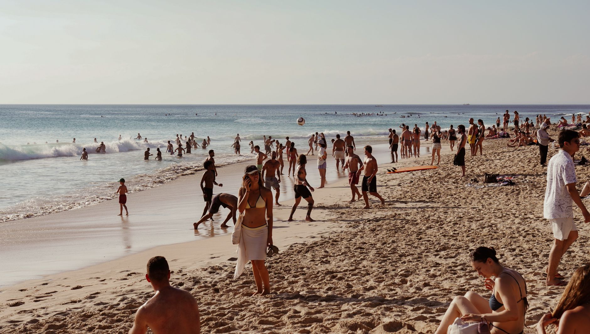 Pessoas aproveitando um dia ensolarado em uma praia lotada em Bali, Indonésia.
