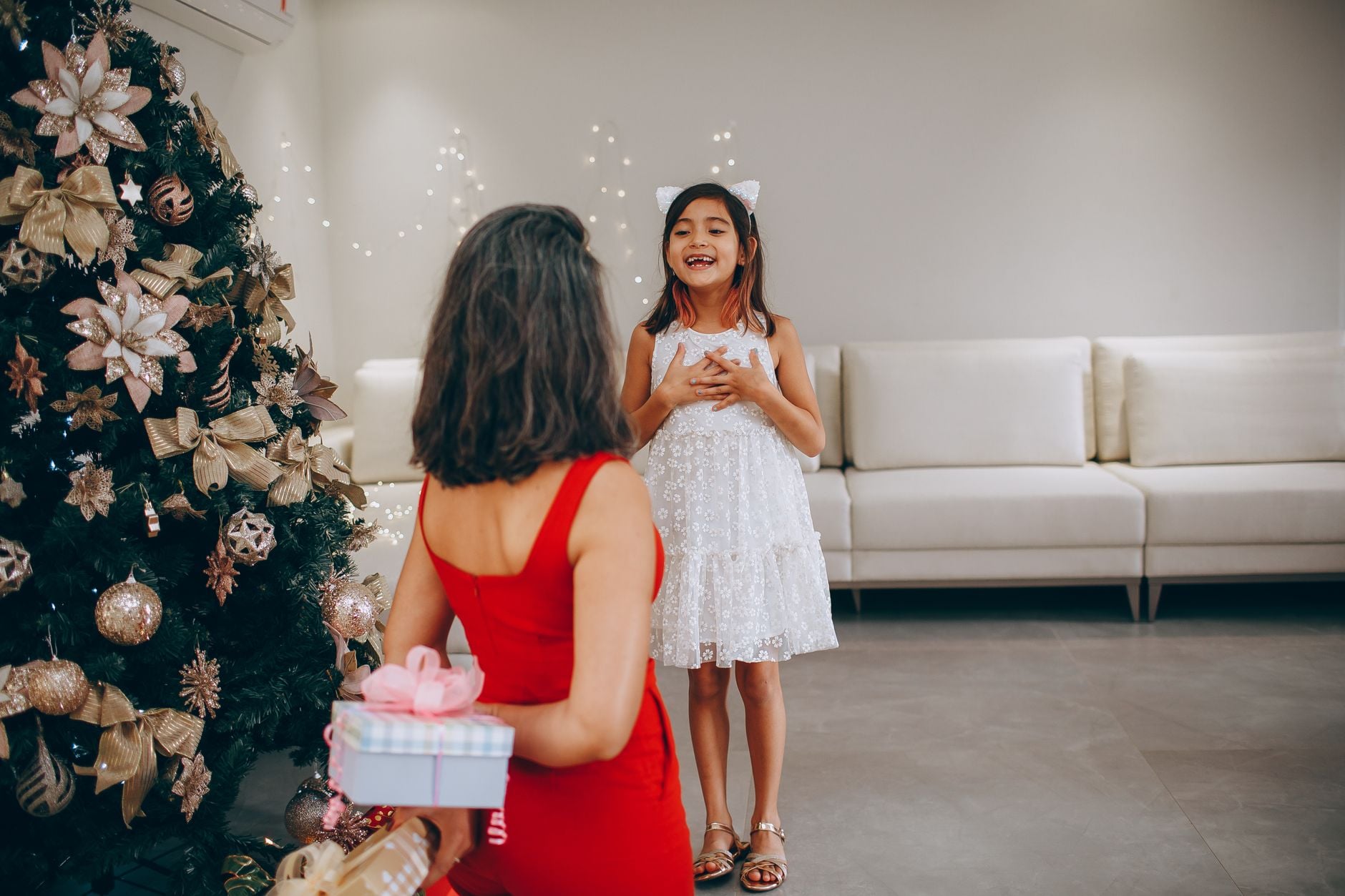 Um momento alegre enquanto uma mãe surpreende sua filha com um presente de Natal ao lado da árvore.