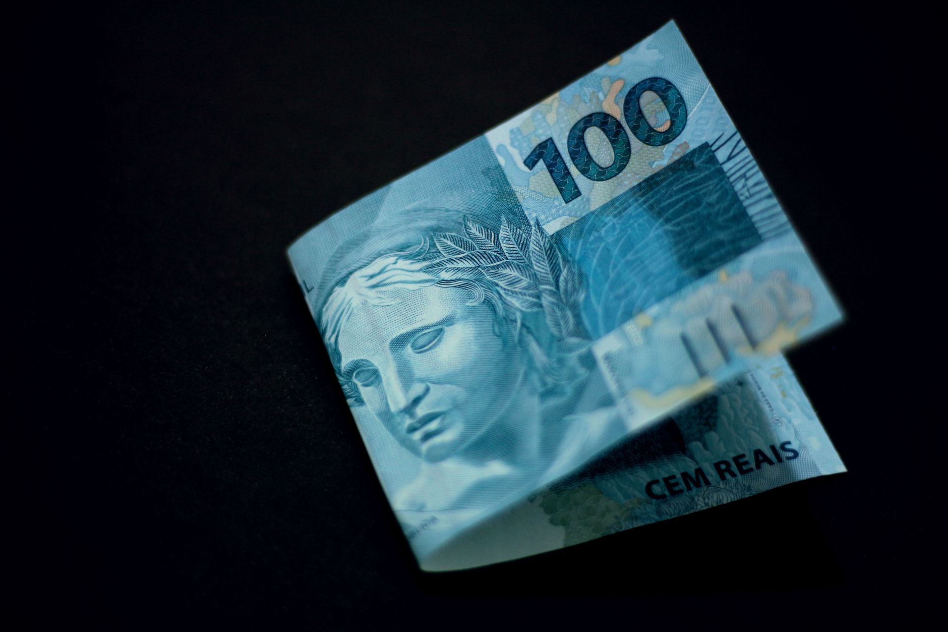 Quanto um deputado estadual recebe por mês para exercer o mandato no Brasil? 1 Uma nota de 100 reais brasileira exibida contra um fundo preto, destacando seu design e cor.
