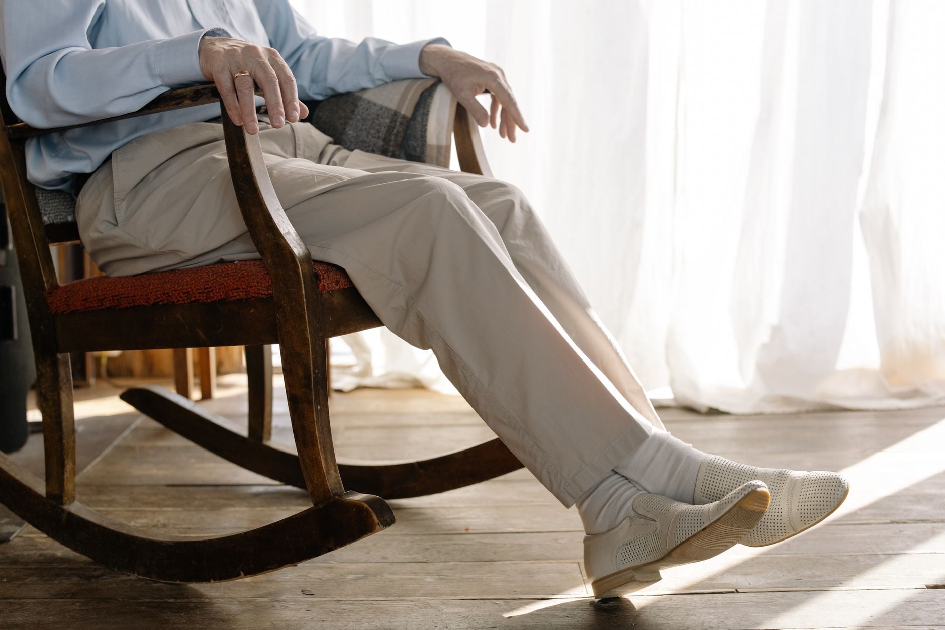 Idoso sentado confortavelmente em uma cadeira de balanço perto de uma janela, exalando relaxamento e calor em ambiente interno.