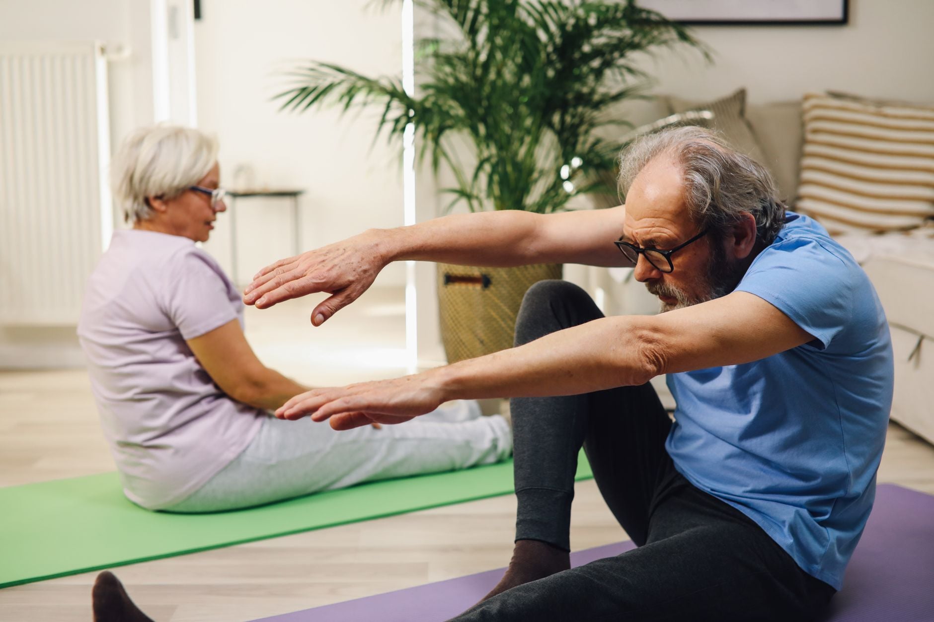 Casal idoso praticando yoga em ambiente interno com foco em bem-estar e fitness.