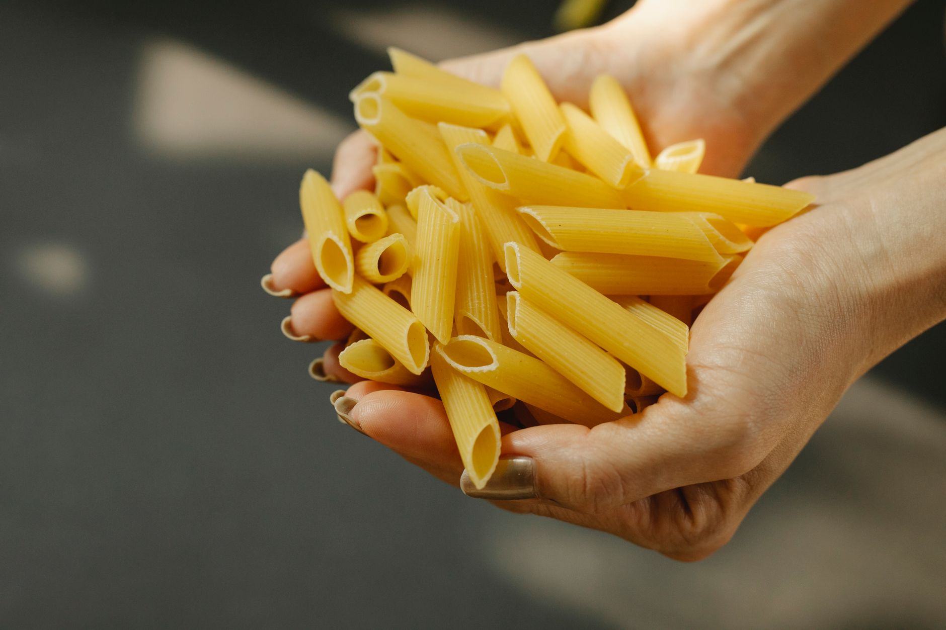 Segundo chefs italianos, este é o único tipo de massa que vale a pena comprar no supermercado 3 Close-up de mãos segurando massa penne crua, enfatizando frescor e apelo culinário.
