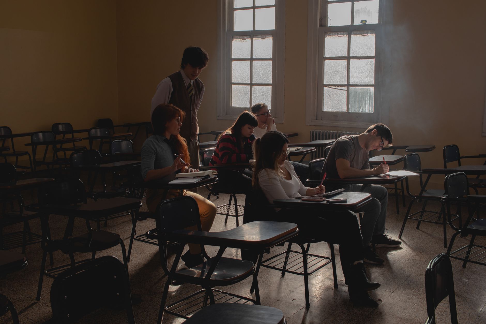 Universidade alegou que as aulas de um professor foram canceladas e ele ficou 20 meses sem receber salário e sem ter turmas para dar aulas, agora, decisão determina pagamento dos valores atrasados e mais R$ 5 mil por danos morais 1 Grupo de estudantes estudando em uma sala de aula com pouca luz, carteiras antigas e luz natural.