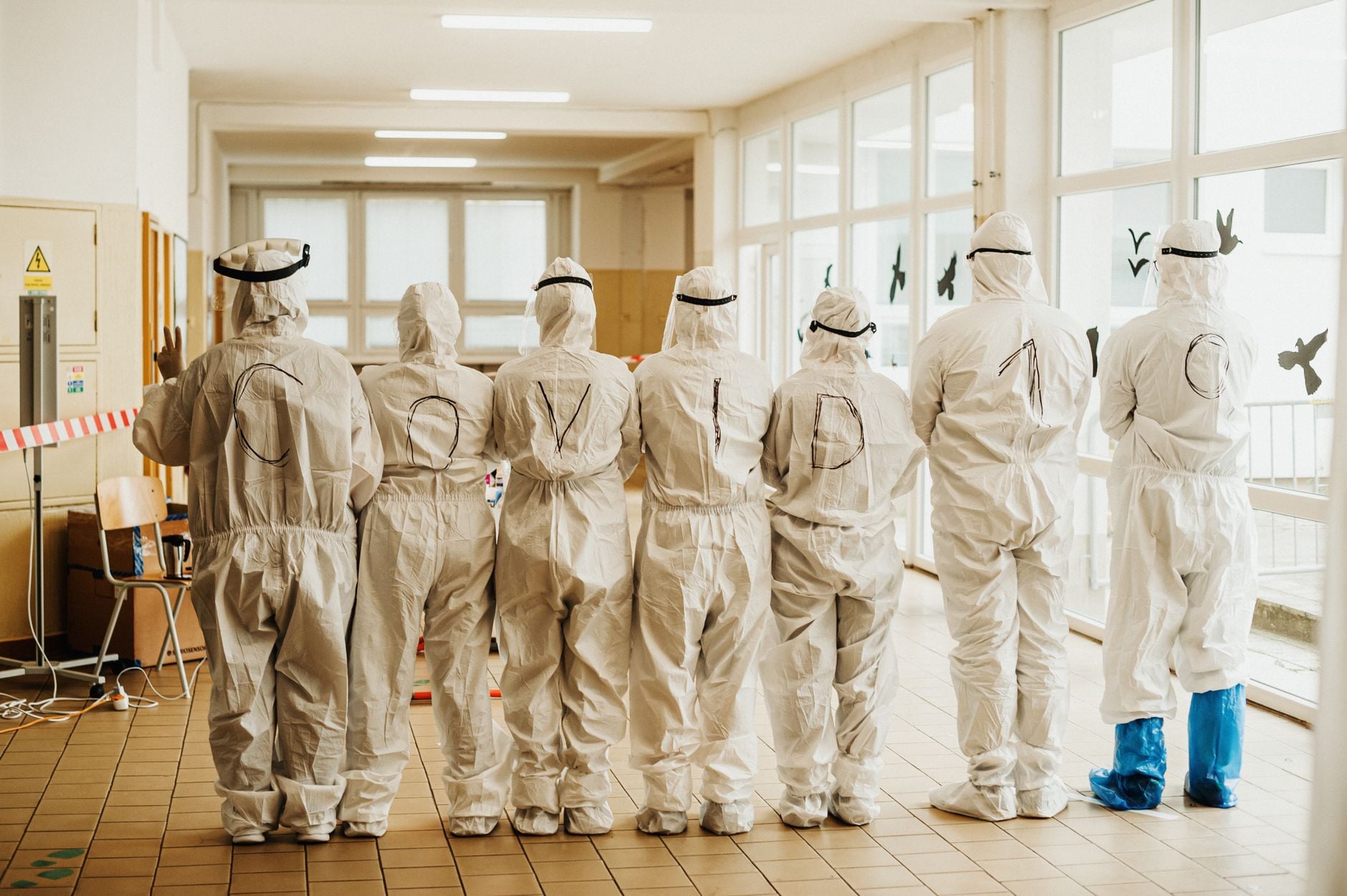 Vírus conhecido por infectar animais foi detectado em um ser humano pela primeira vez em um país da Europa 2 Profissionais de saúde em trajes de EPI com texto COVID-19, vista traseira, indoors.