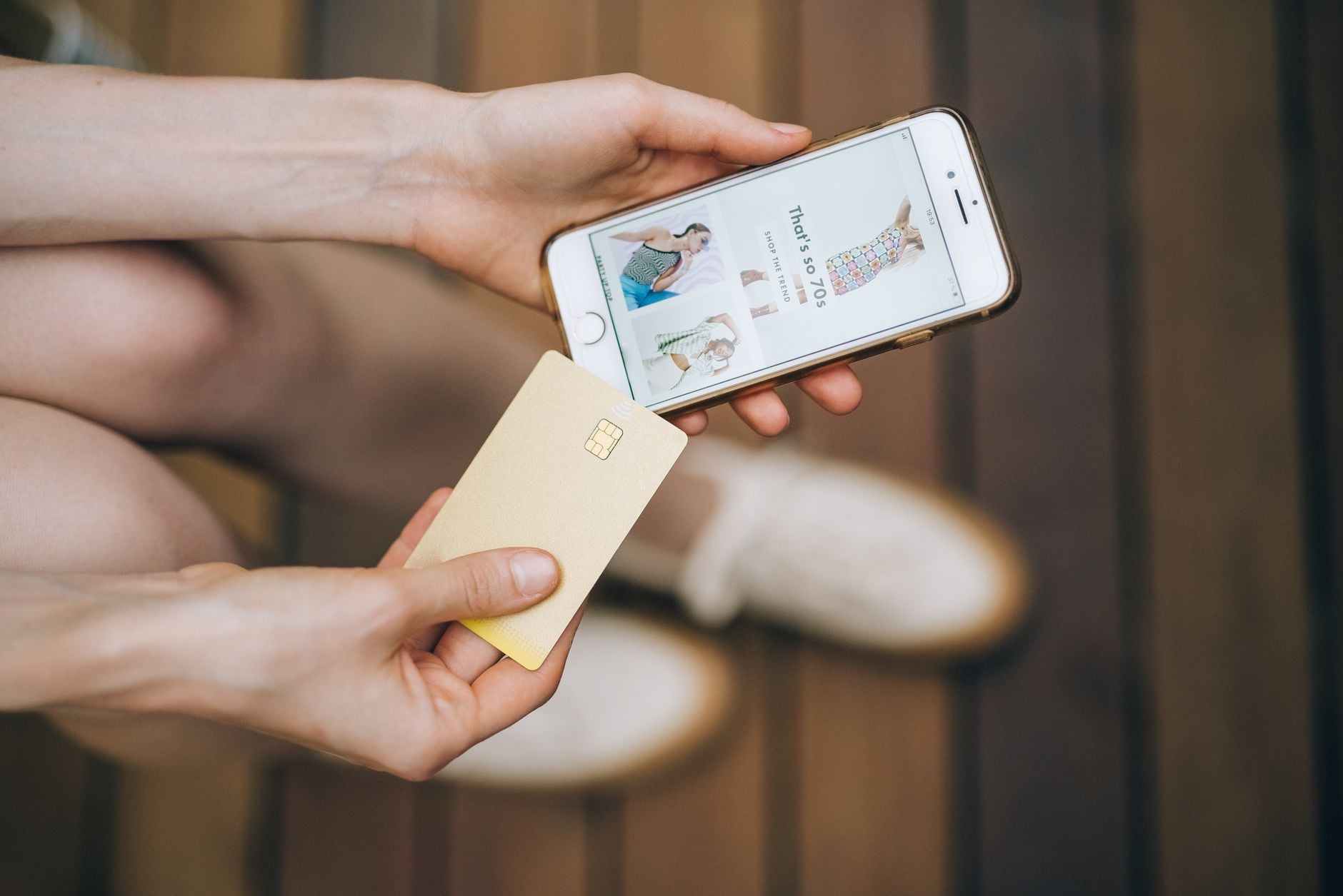 Você comprou roupas pela internet nos últimos dias? Ataque a lojas brasileiras capturava cartões e CPFs durante o pagamento 2 Mãos segurando smartphone e cartão de crédito para compras online em um piso de madeira.