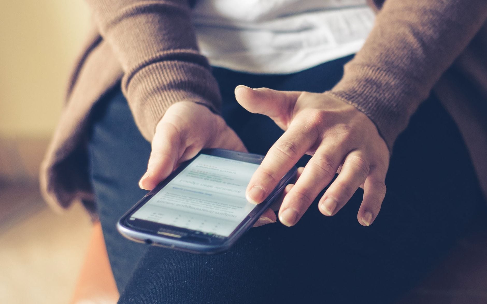Você conversa sobre um produto e, pouco depois, aparece um anúncio dele no celular; será que os aplicativos estão ouvindo suas conversas? Veja como descobrir 2 Close-up de um adulto usando smartphone em ambientes internos, navegando na web com foco na tela.