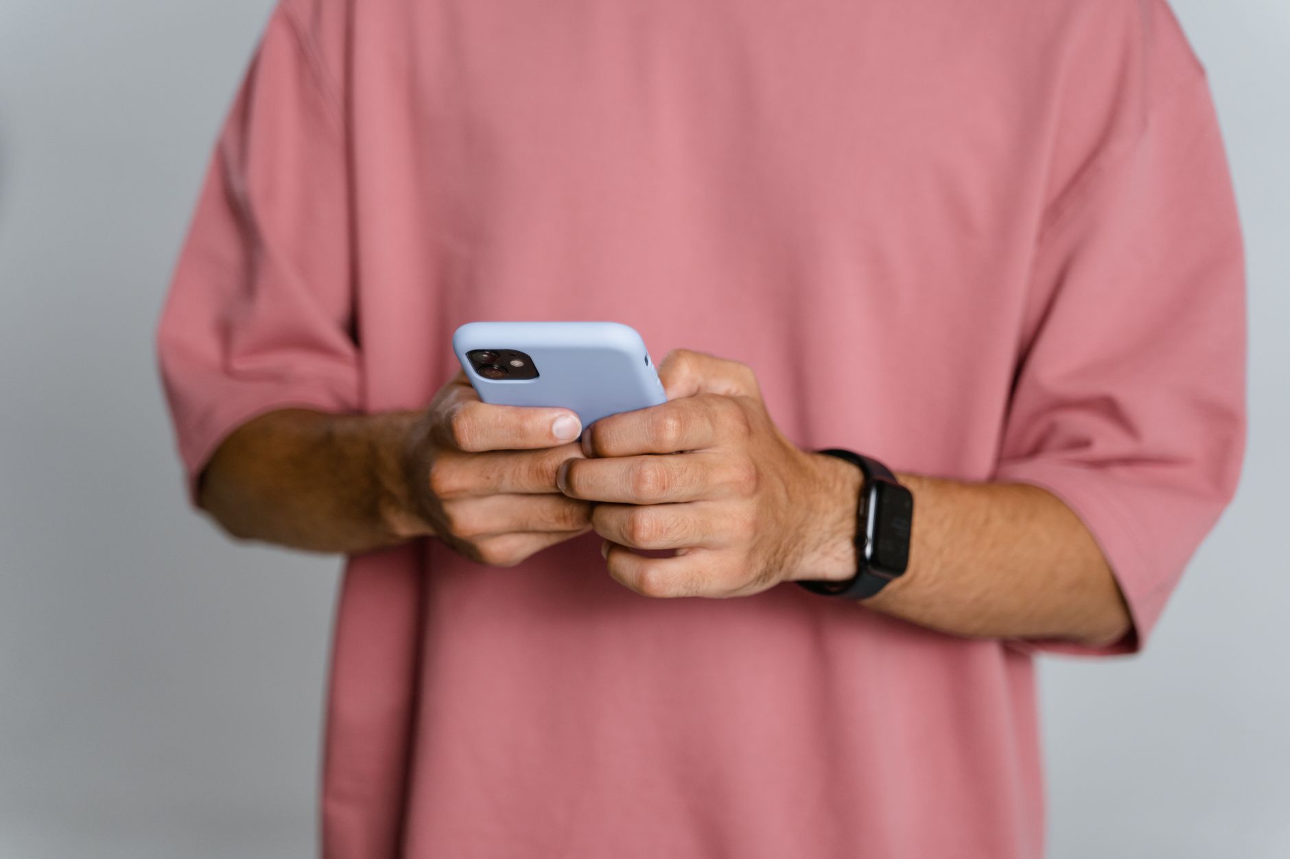 Você conversa sobre um produto e, pouco depois, aparece um anúncio dele no celular; será que os aplicativos estão ouvindo suas conversas? Veja como descobrir 3 Homem adulto em camiseta rosa usando smartphone; foco nas mãos e no telefone.