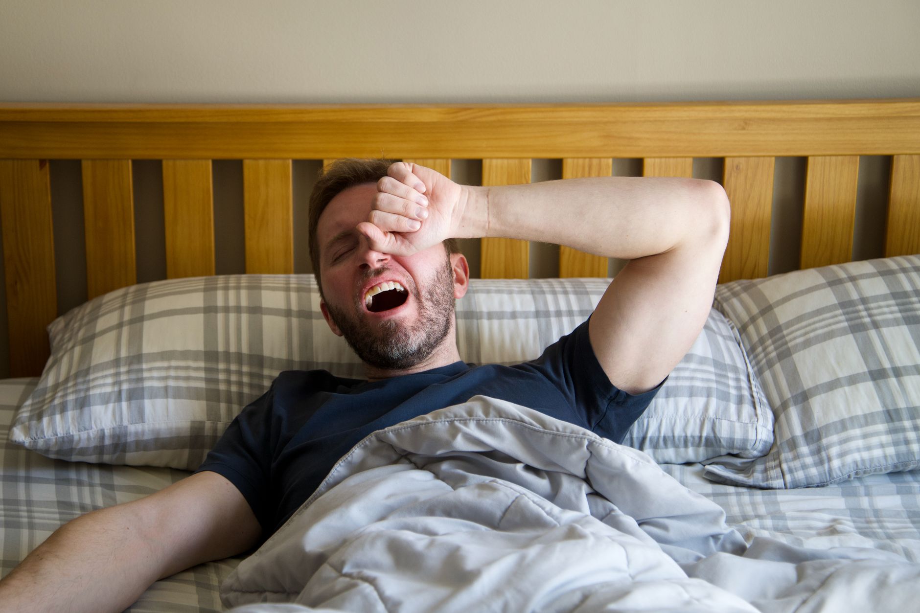 Você costuma dormir depois do almoço e acorda ainda mais cansado? Especialista explica quanto tempo deve durar o cochilo da tarde e por que passar alguns minutos a mais pode atrapalhar sua disposição e o sono da noite 2 Homem bocejando e acordando na cama, começando um novo dia com a luz da manhã.