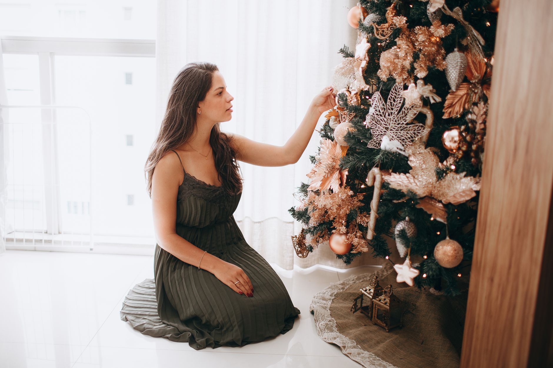 Mulher decorando uma árvore de Natal festiva dentro de casa, adicionando enfeites.