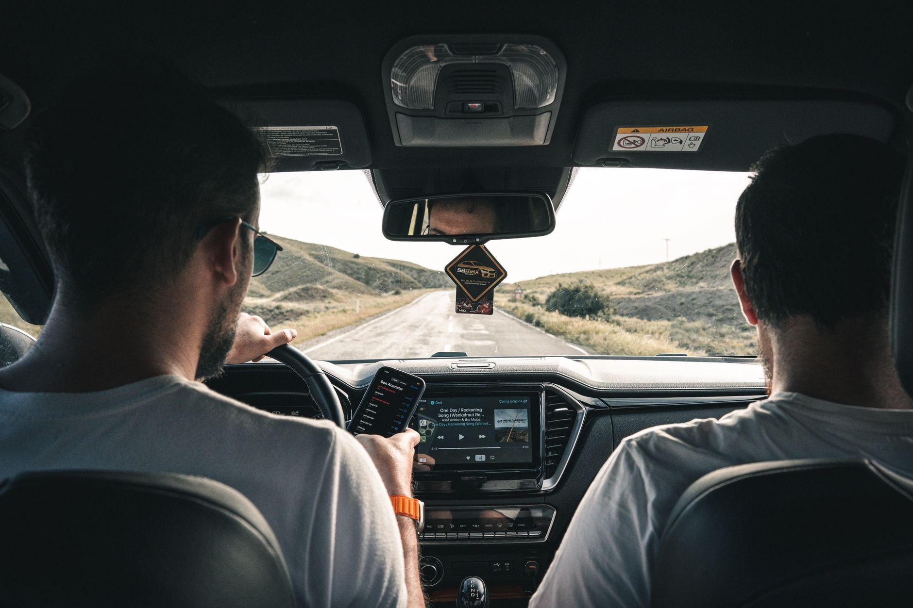 Dois homens dirigindo por uma paisagem cênica, usando um celular para navegação.